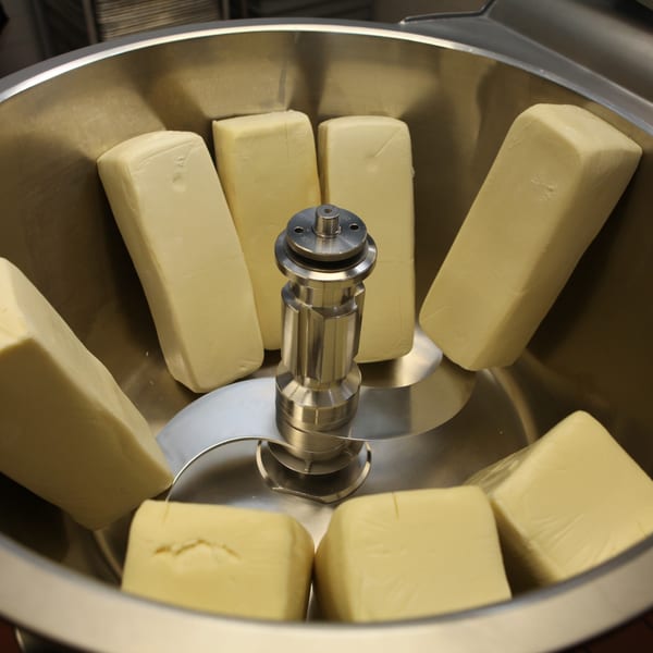 Blocks of cheese in a large metal mixer, ready to be shredded for Harris Pizza.