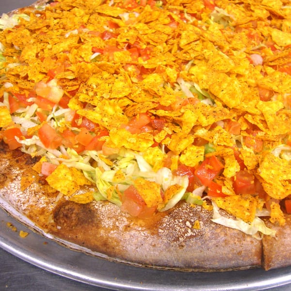 Close-up of a Harris Pizza taco pizza topped with Doritos, lettuce, and diced tomatoes.