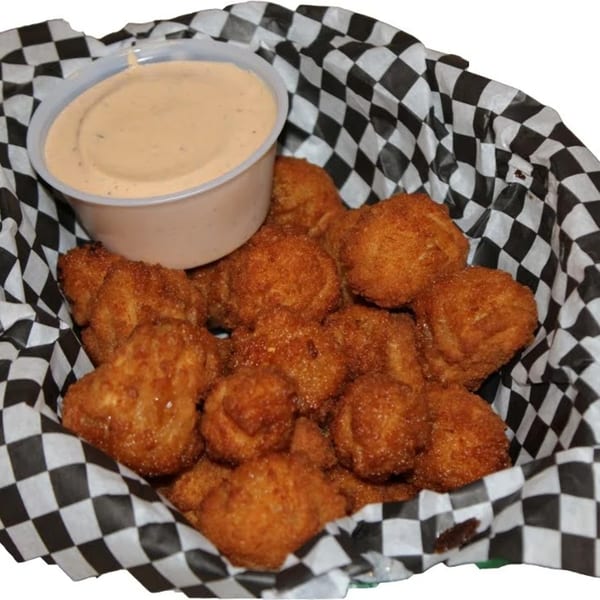 A basket of golden-brown fried appetizers with a side of dipping sauce in a checkered paper lining.