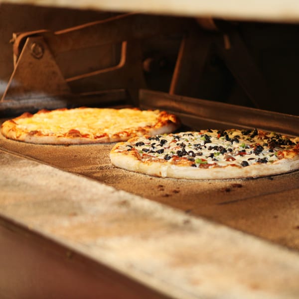 Two Harris pizzas, one cheese and one with black olives, baking inside a hot oven.
