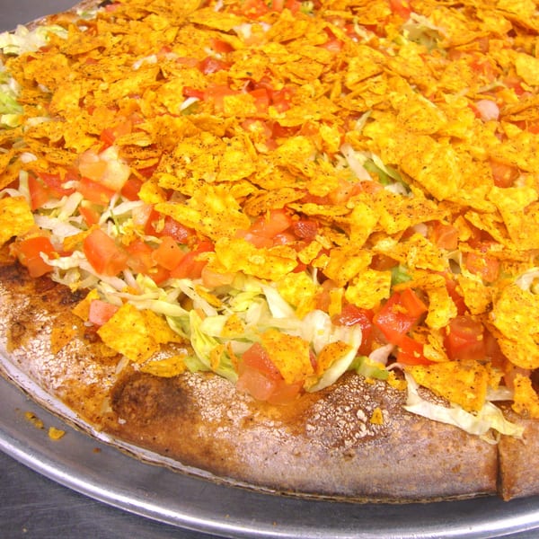 Close-up of a Harris Pizza taco pizza topped with Doritos, lettuce, and diced tomatoes.
