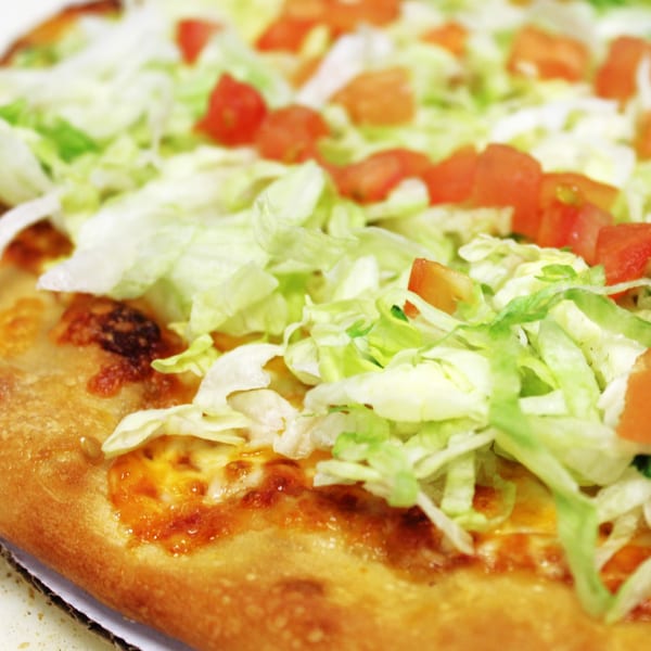 Close-up of a Harris Pizza taco pizza topped with shredded lettuce and diced tomatoes.