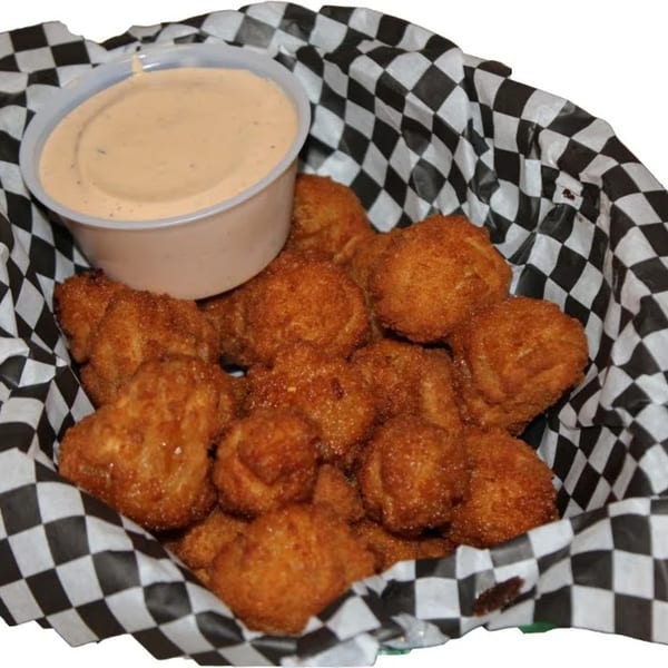 A basket of golden-brown fried mushrooms with a side of dipping sauce in a checkered paper liner.