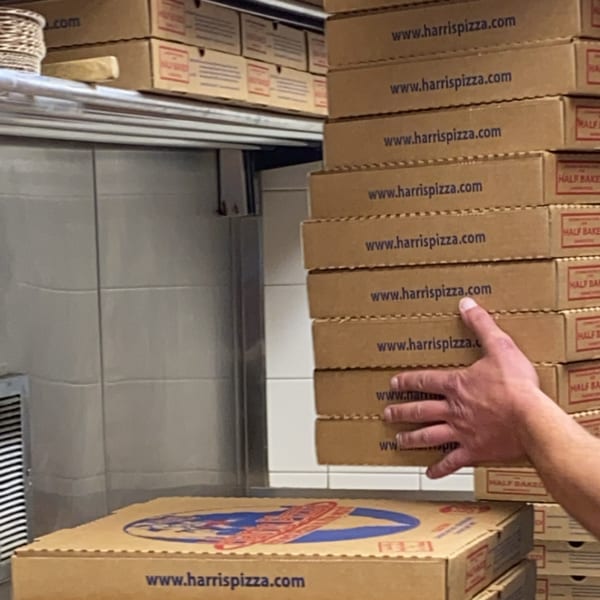 A hand stacks numerous Harris Pizza boxes, ready for delivery or pickup.