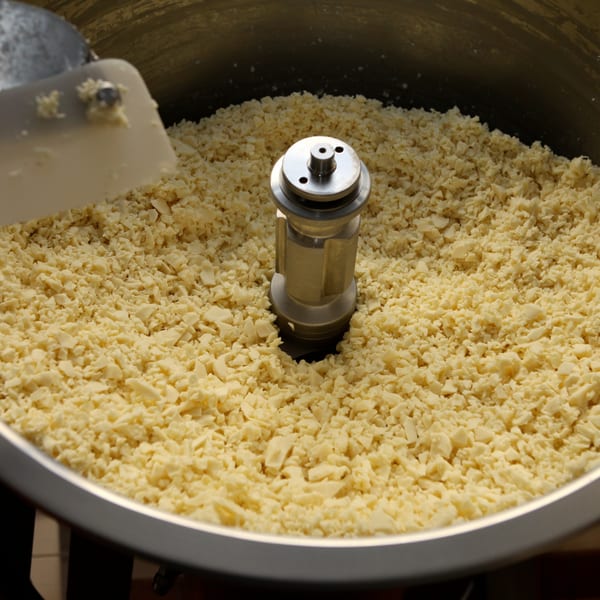 A large metal bowl filled with shredded cheese, with a mixer attachment visible in the center.