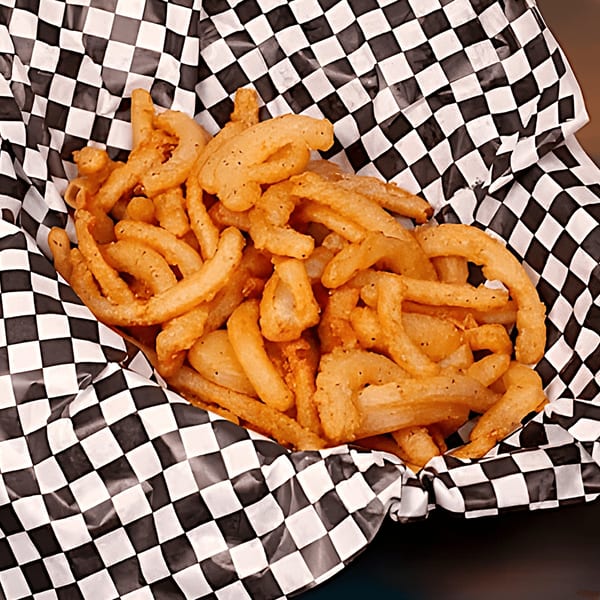 Golden curly fries seasoned with pepper, served in a black and white checkered paper basket.