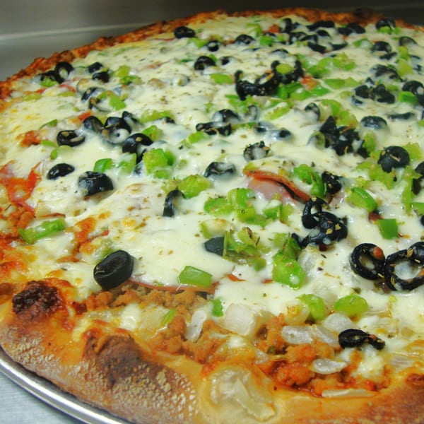 A close-up of a Harris Pizza with melted cheese, black olives, green peppers, and sausage.