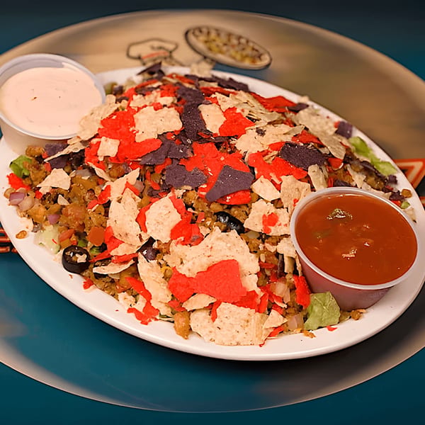 A large plate of nachos with red and blue tortilla chips, ground meat, and two dipping sauces.