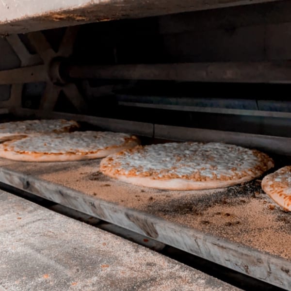 Multiple pizzas with cheese and toppings baking inside a large commercial oven at Harris Pizza.