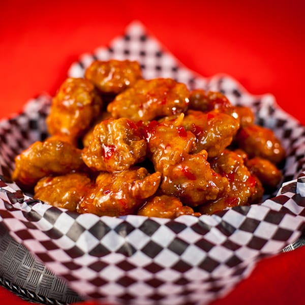 Sweet chili boneless wings in a checkered paper-lined basket against a red background.