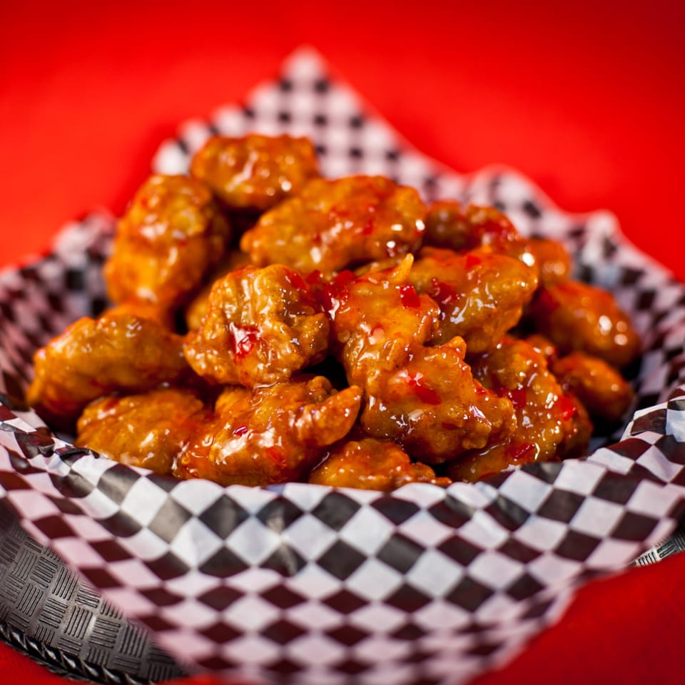 Sweet chili boneless wings in a checkered paper-lined basket against a red background.