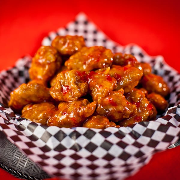 A basket of Harris Pizza's boneless wings, coated in a sweet and spicy sauce, against a red background.