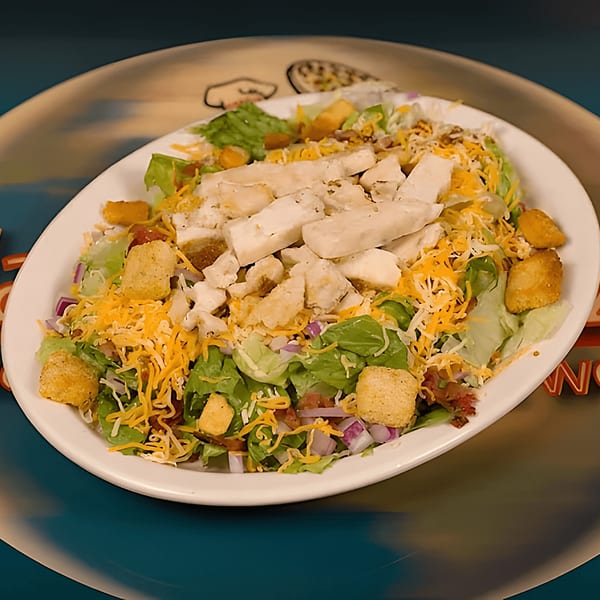 A large salad with chicken, cheese, croutons, and red onion on a white oval plate.