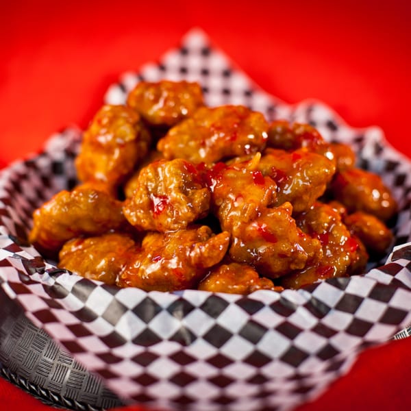 Sweet chili boneless wings in a checkered paper-lined basket against a vibrant red background.