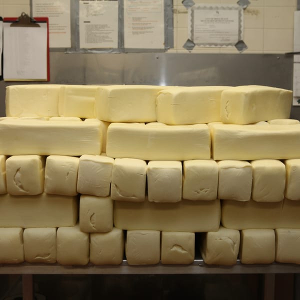 Large blocks of mozzarella cheese stacked on a metal shelf in a pizza kitchen.